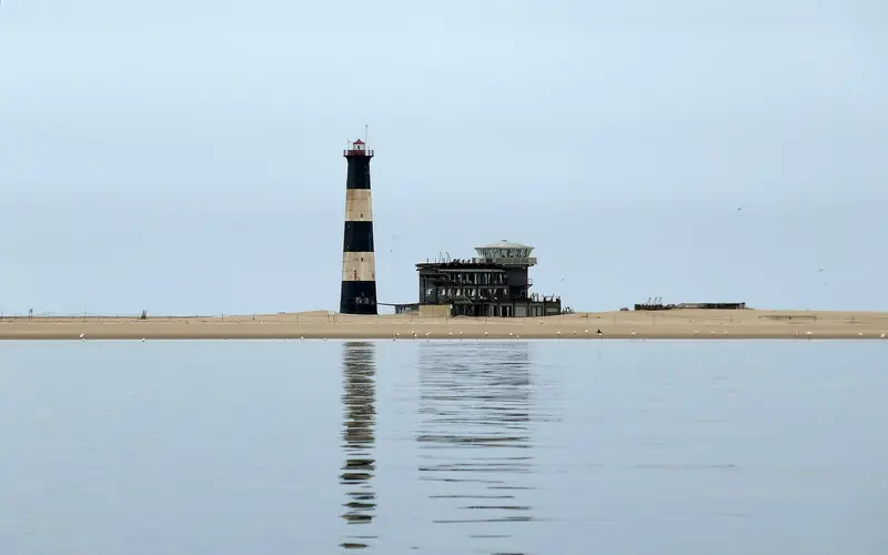 Black-and-white striped Pelican Point lighthouse and lodge on the sand spit, reflected in calm water