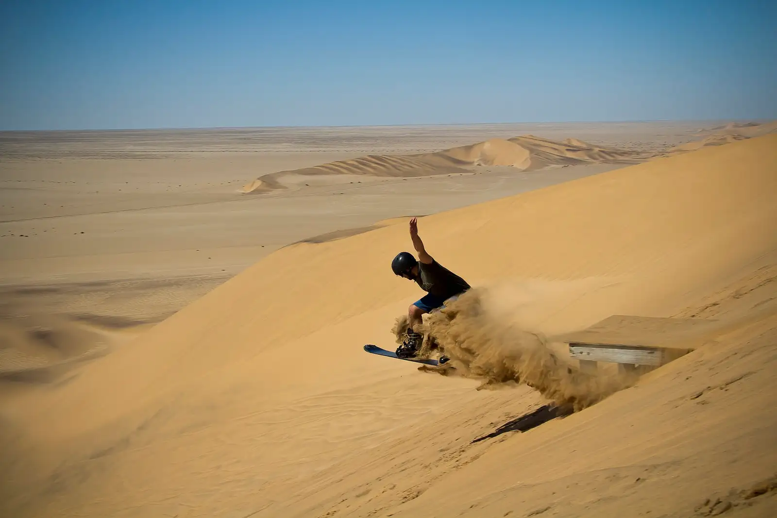 Stand-up sandboarder spraying sand on a dune near Swakopmund