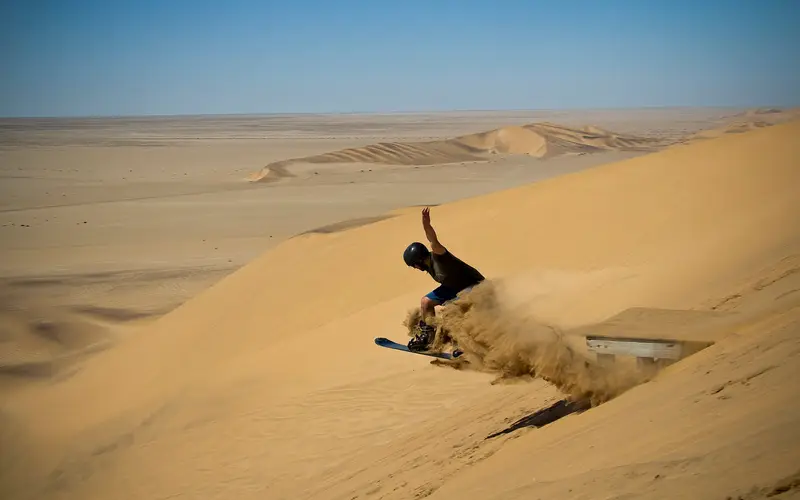 Stand-up sandboarder spraying sand on a dune near Swakopmund